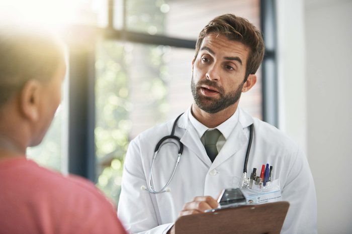 Doctor in a white coat and clipboard talking to a patient.