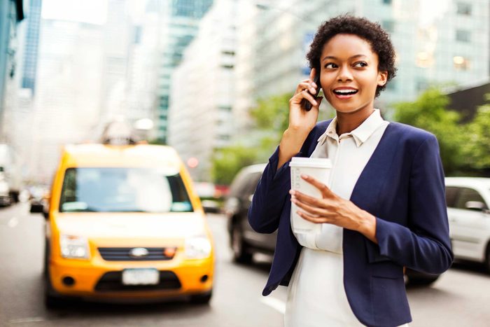woman on street with to-go coffee, talking on cell phone