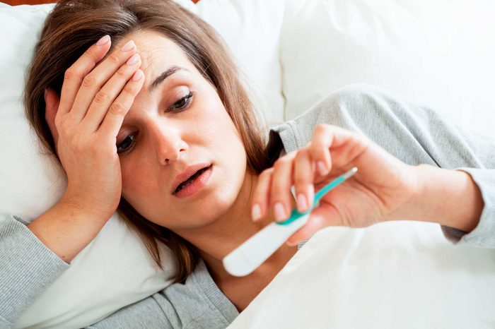 Woman with a fever checking her temperature with a thermometer.
