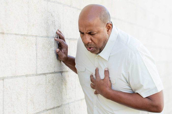 Man in a white shirt clutching his chest and leaning on a wall.