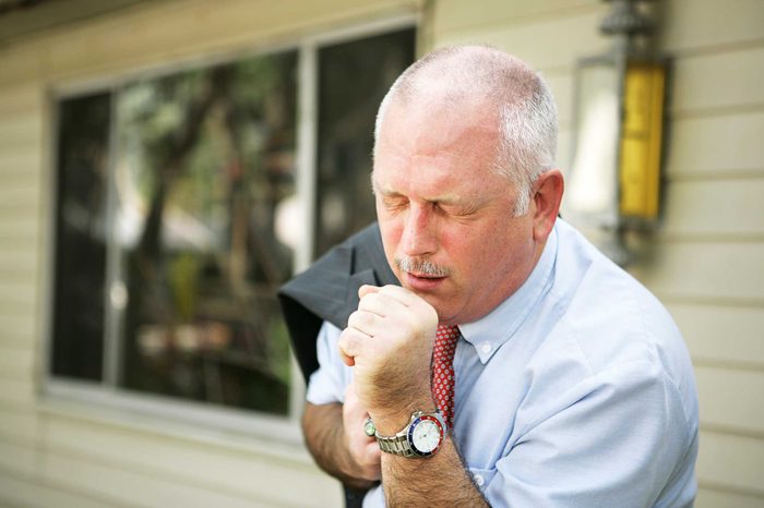 Man in work dress coughing into his hand.